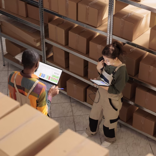 Storehouse worker doing products inventory on tablet computer, inspecting goods during quality control in storage room. Shipping company employees packing boxes, discussing cargo audit. Top view